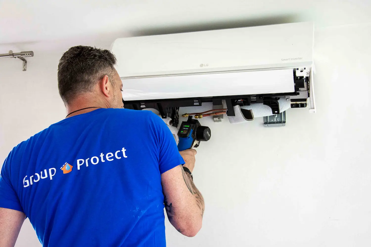 Technicus monteert de binnenunit van een lucht-luchtwarmtepomp aan een witte muur in een woning.