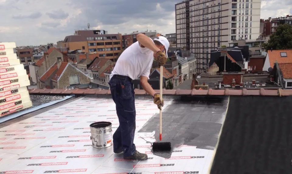 Dakwerker brengt de waterdichtingslaag aan op de isolatieplaten van een plat dak in renovatie.
