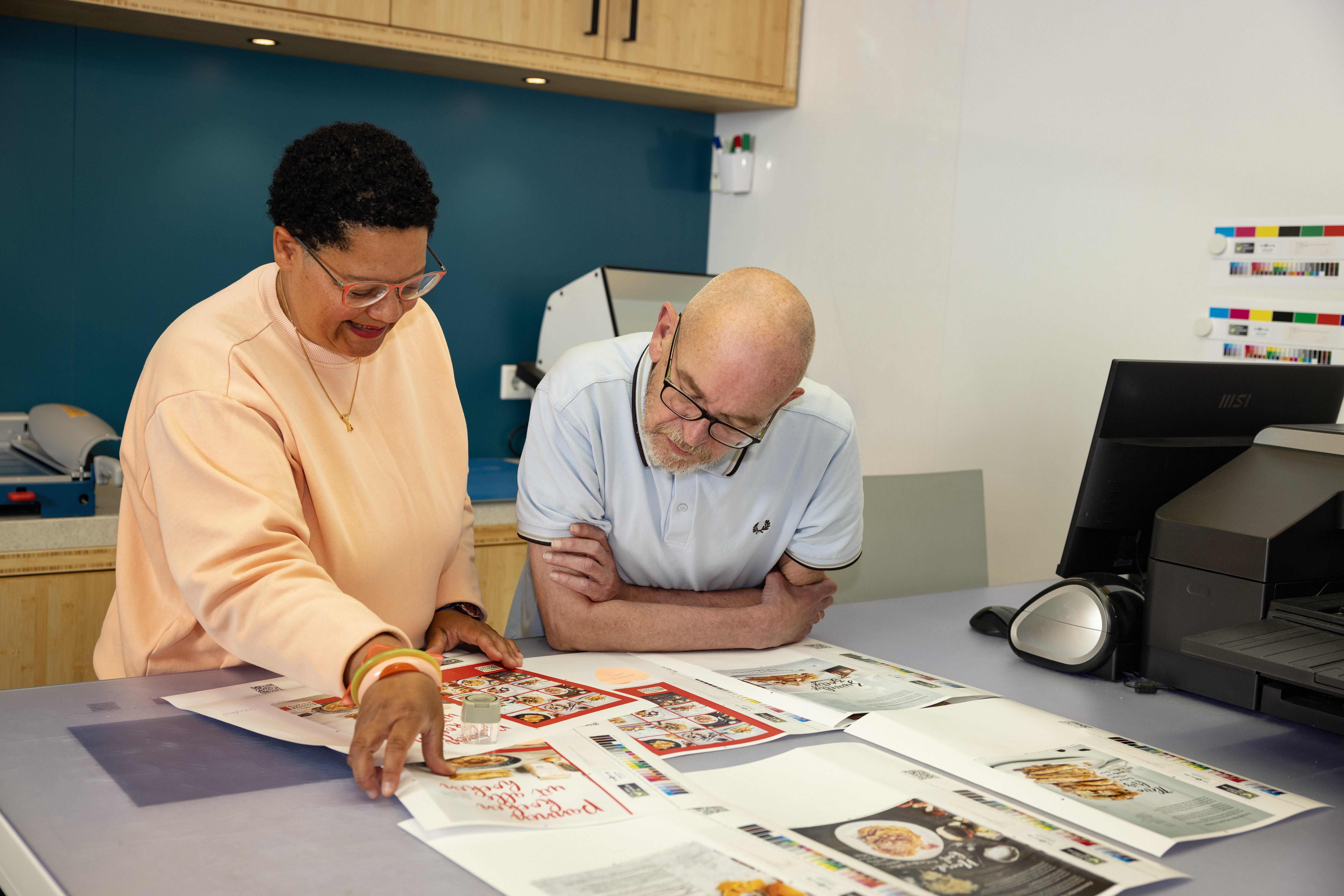 Two people reviewing printed color proofs on a table in a print shop or design studio.