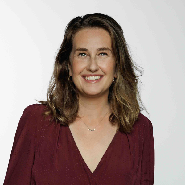 Smiling woman with shoulder-length brown hair wearing a burgundy V-neck blouse against a plain light background.