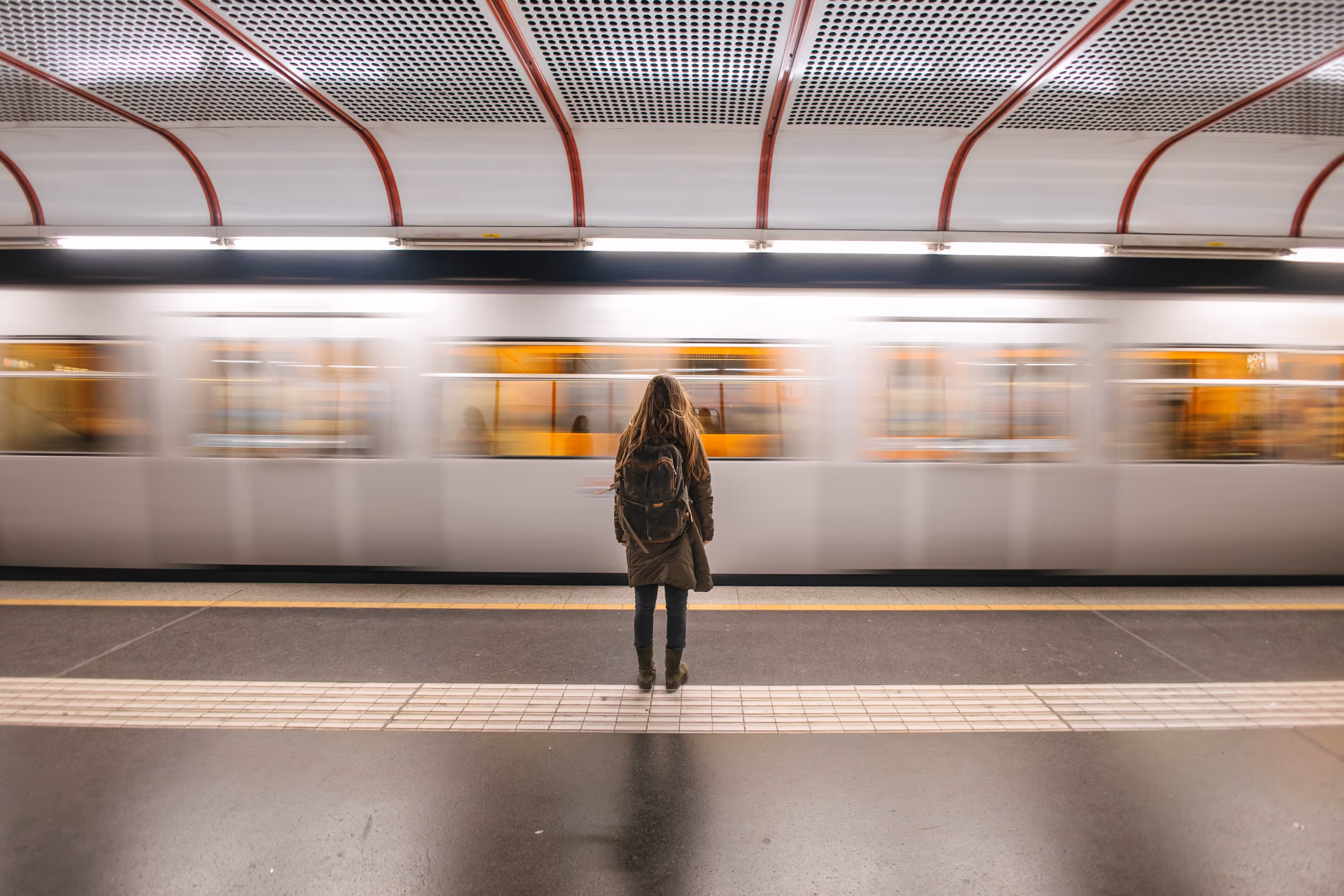 Femme de dos sur un quai de métro, attendant ou observant un train en mouvement, symbolisant la mobilité urbaine.