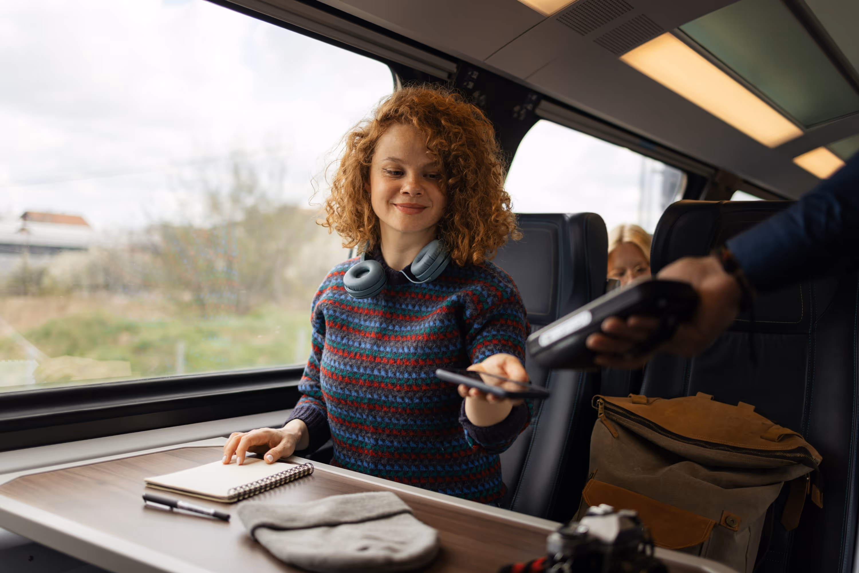 Voyageuse souriante payant son billet de train par application mobile, représentant la billettique moderne et l'ingénierie des systèmes.