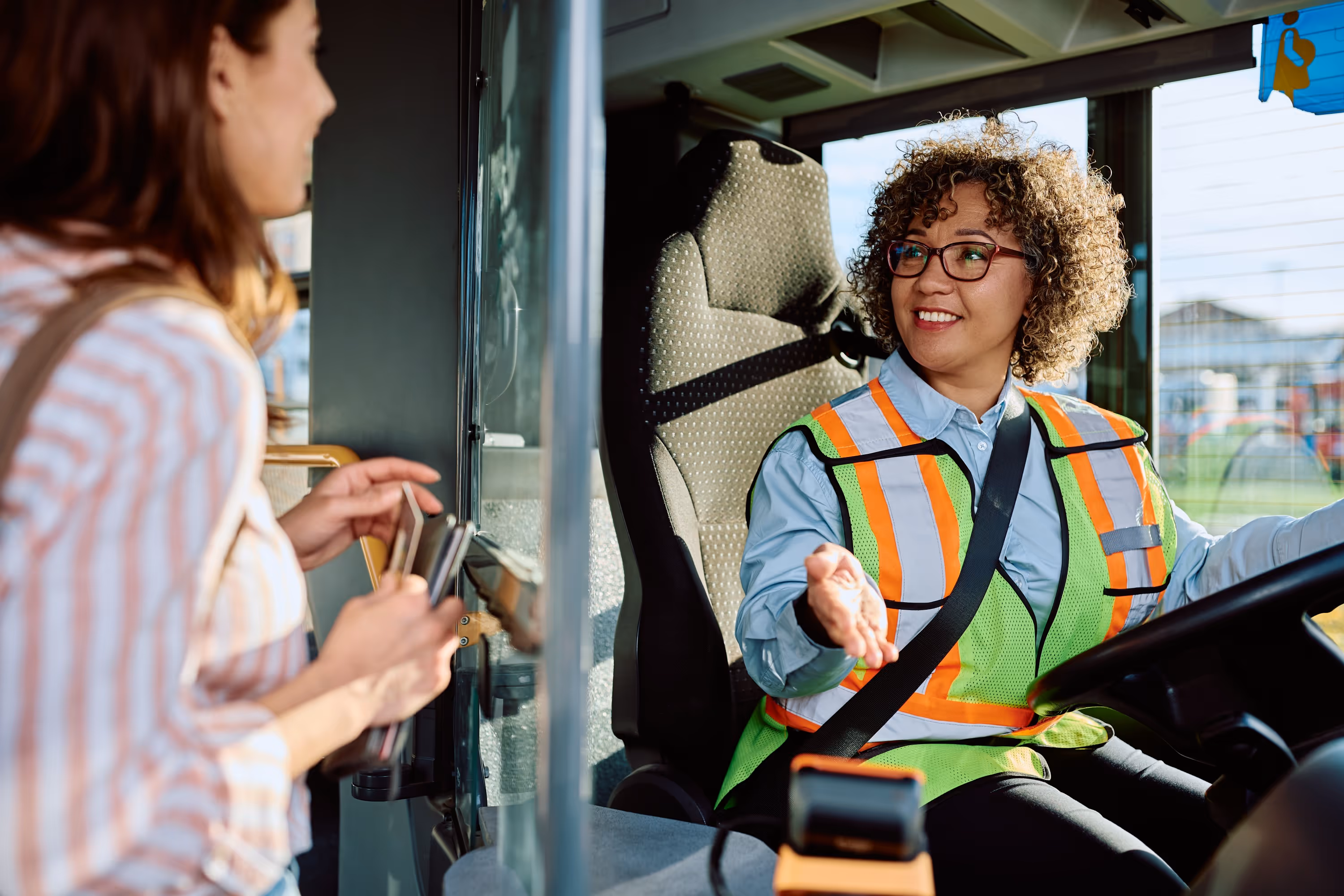 Conductrice de bus souriante interagissant avec une passagère utilisant son téléphone pour le paiement, illustrant le service et la billettique.