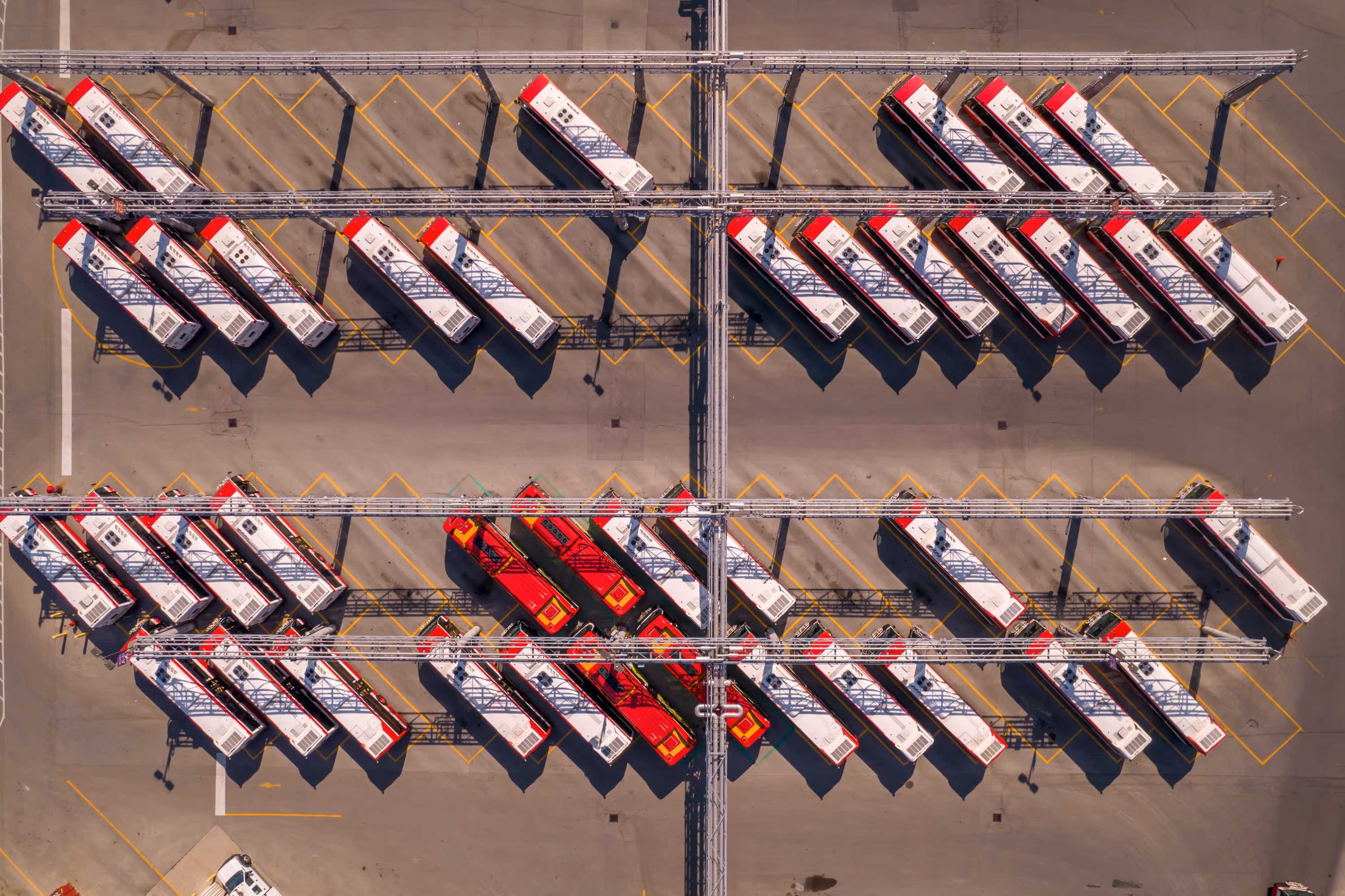 Vue aérienne d'un grand dépôt d'autobus avec de nombreux véhicules rouges et blancs garés, illustrant la gestion d'infrastructures.