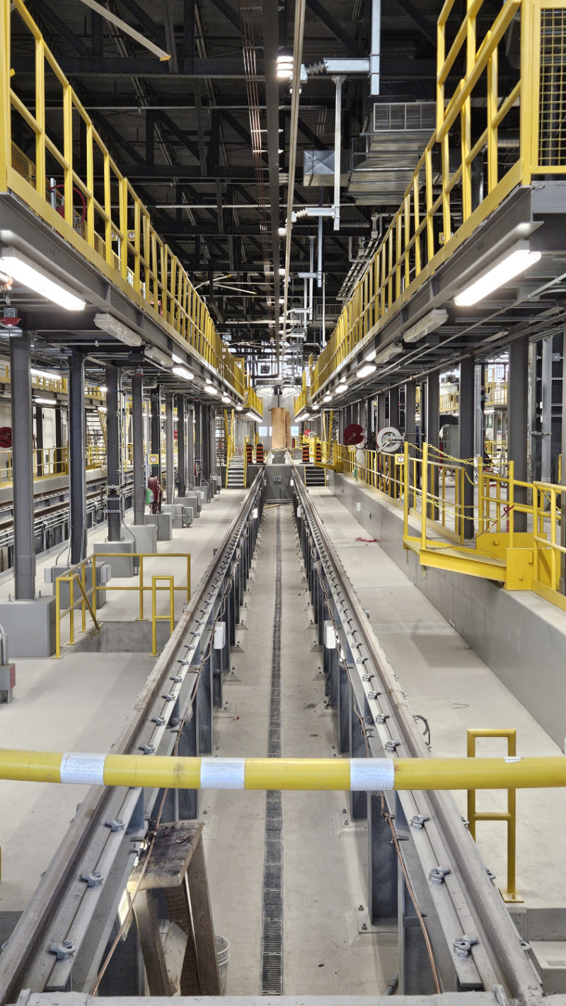 Intérieur d'un dépôt de maintenance ferroviaire avec voies de tram ou métro et balustrades jaunes.