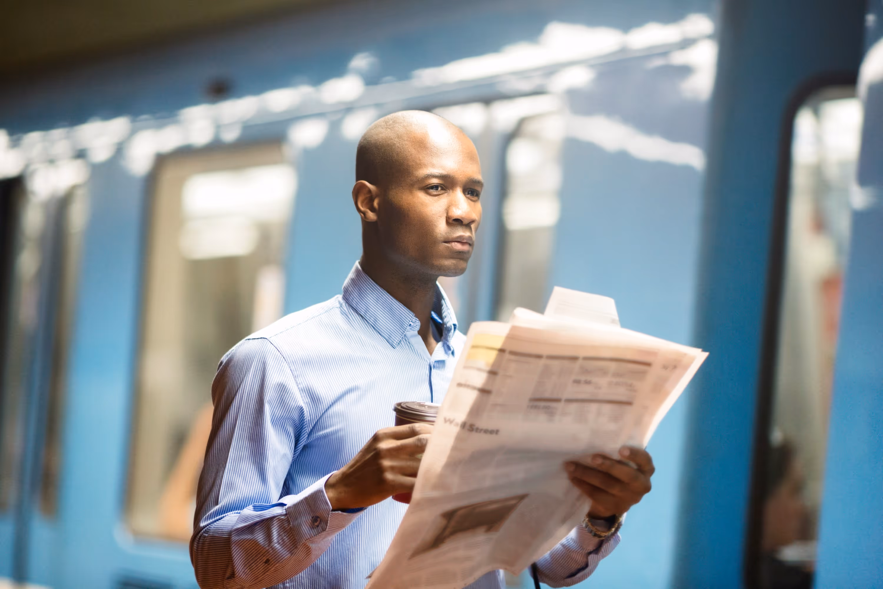 A professional man holding a newspaper and coffee cup, standing in what appears to be a subway or train car, indicating urban commute and efficiency.
