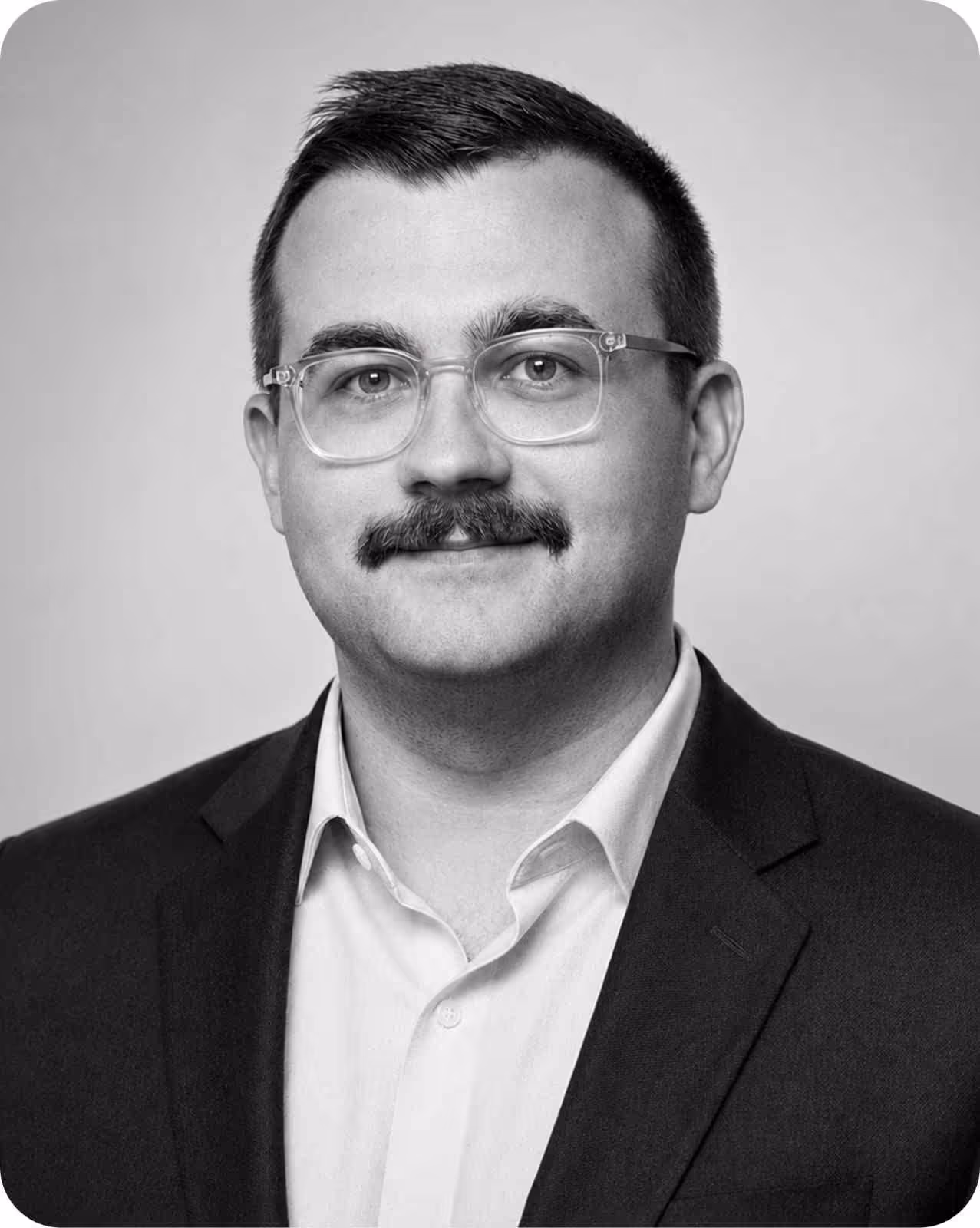 Portrait of a man with glasses and mustache wearing a suit jacket and collared shirt.