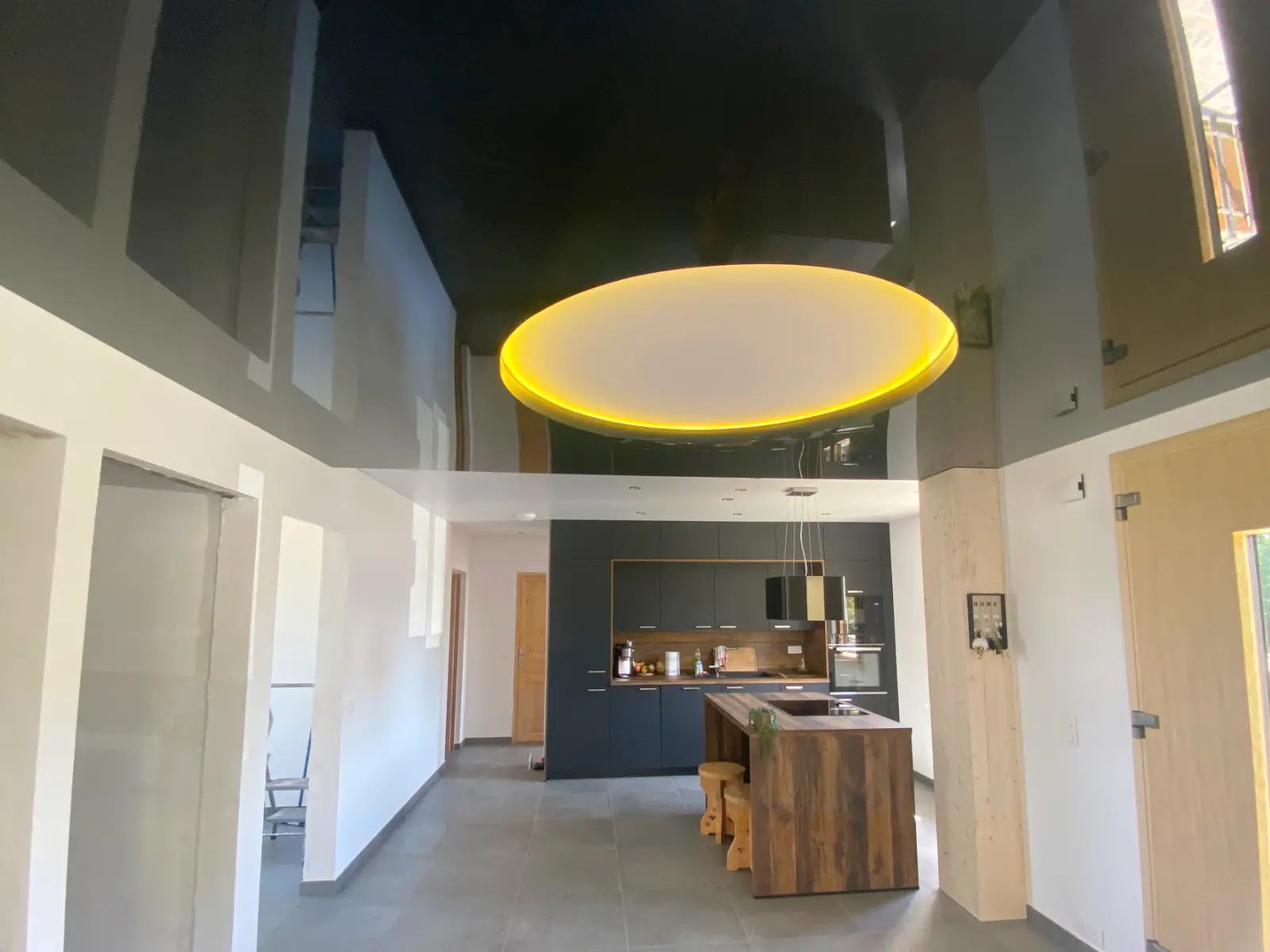 Plafond tendu noir brillant avec des reflets et un grand luminaire rond - vue rapprochée