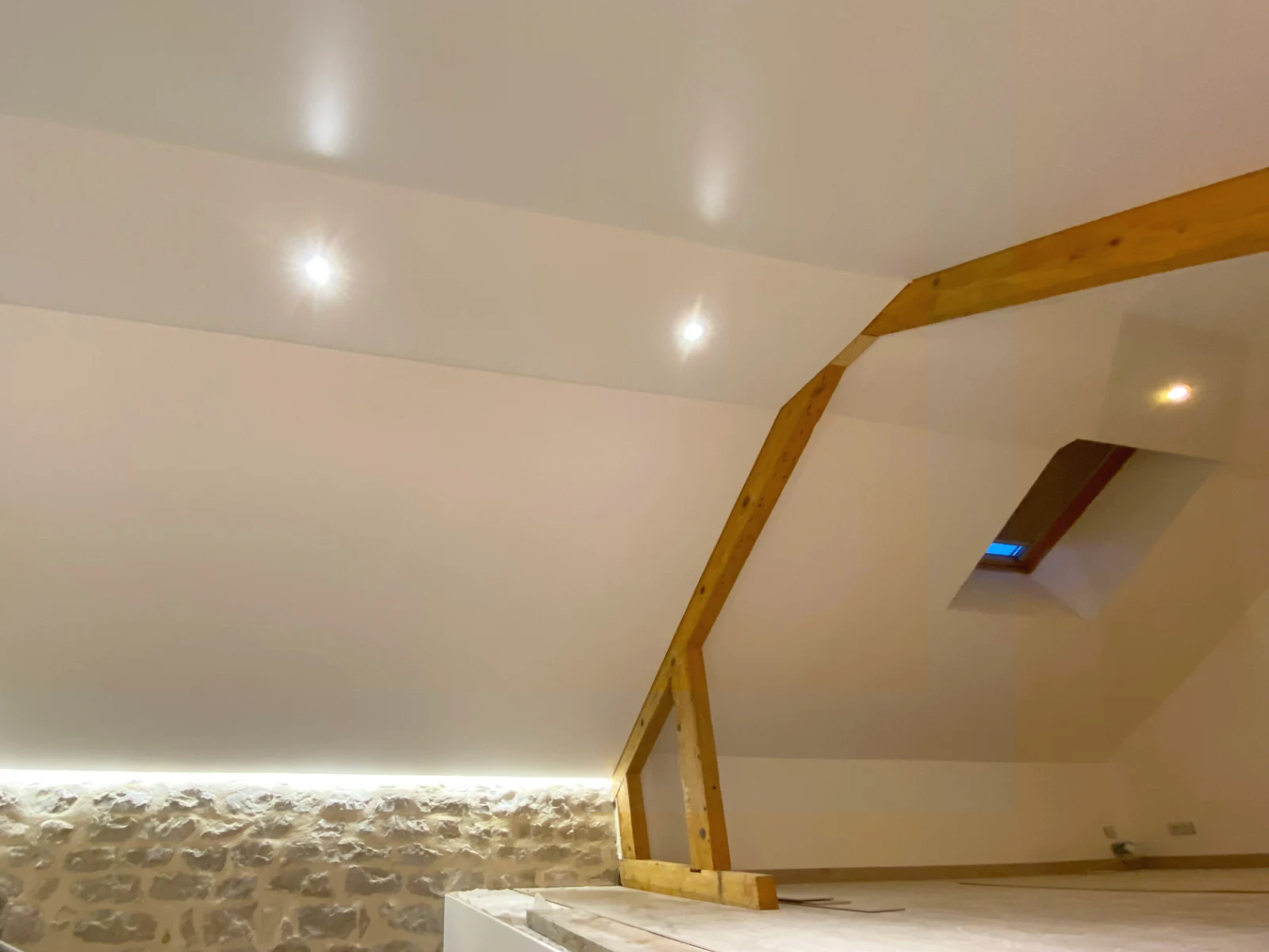 Faux-plafond dans une sous-pente rénovée, mur en pierre et luminaire encastrés