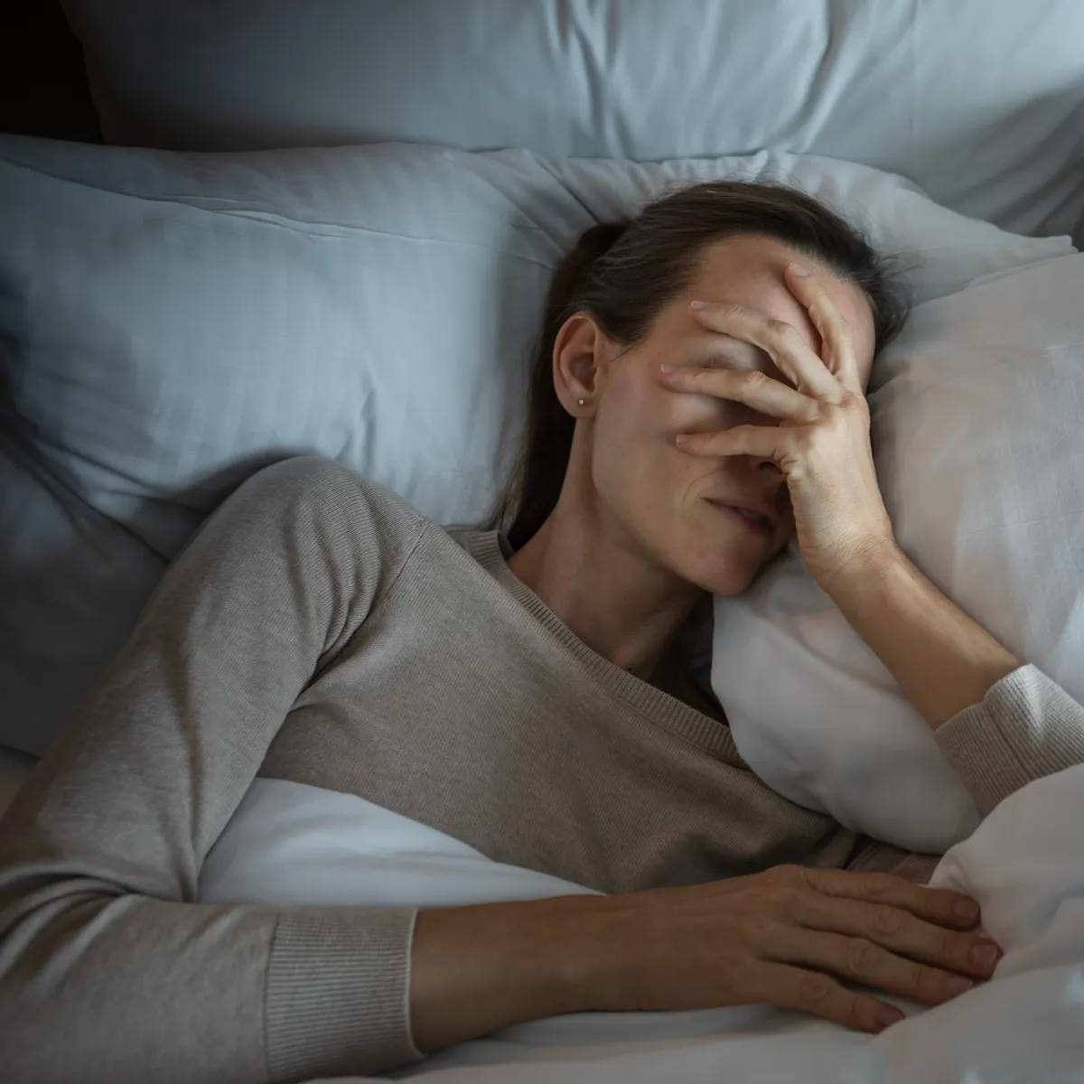 Frau liegt erschöpft im Bett und leidet unter Schlafproblemen und Rückenschmerzen