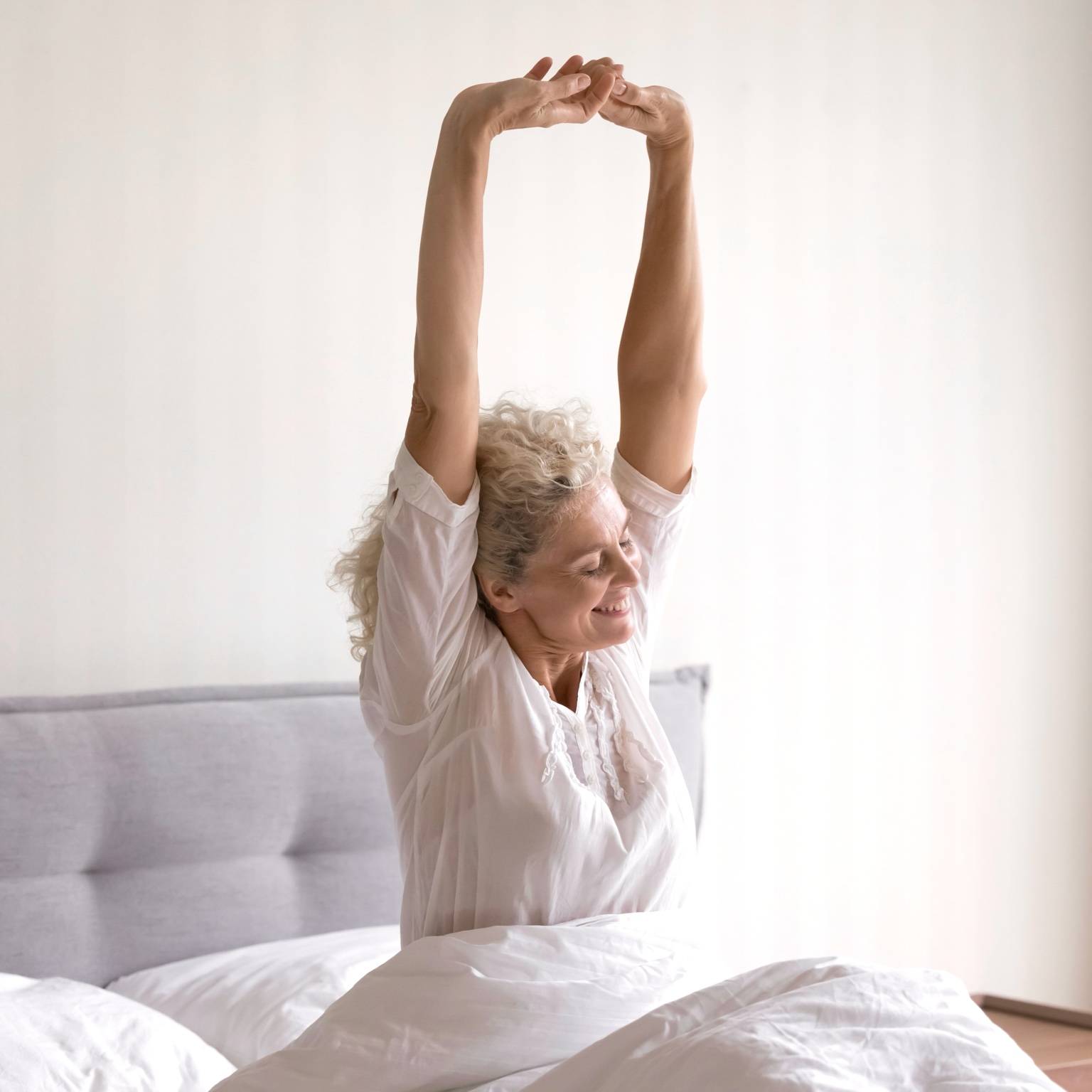 Ältere Frau wacht erholt auf und streckt sich nach gesundem Schlaf auf massgefertigter Matratze