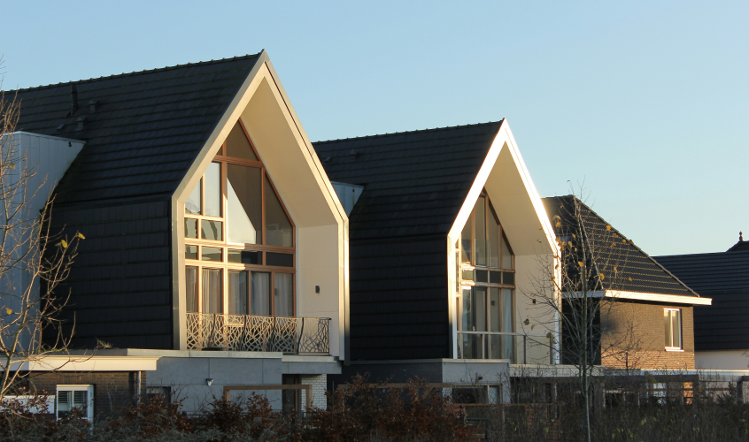 Two modern houses with steep black roofs and large triangular windows reflecting sunlight.