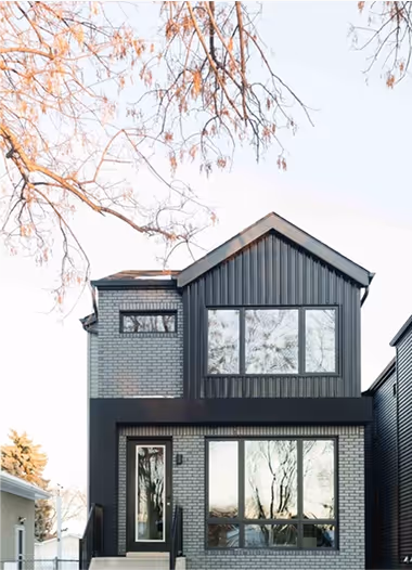 Modern two-story house with black and gray brick exterior and large windows reflecting trees.