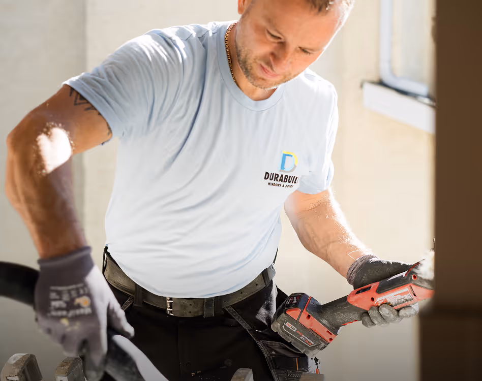 Man wearing a light blue DURABUILT t-shirt and gloves operating a red power tool indoors.
