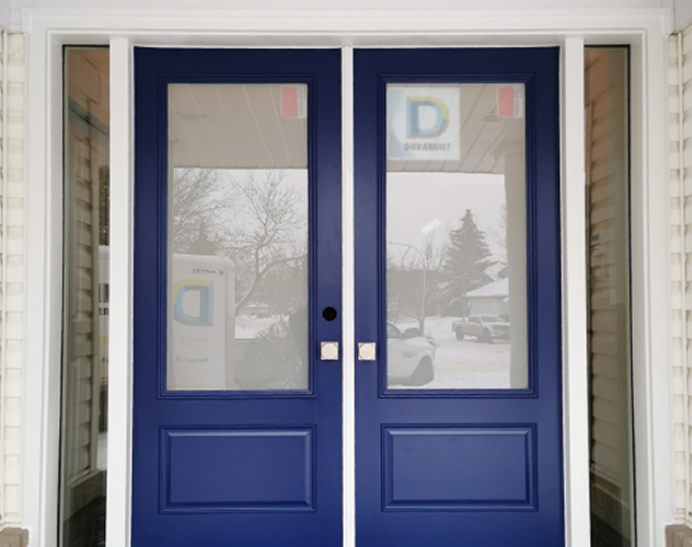 Front view of a double blue door with large glass panels and silver square handles, showing a snowy outdoor scene reflected in the glass.