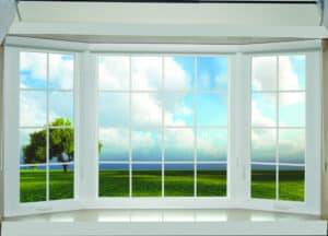 An expansive bay window looking out to a field and tree.