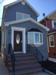 A home in a New York neighborhood with a stoop, brown door, and blue siding