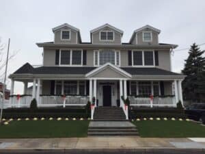 A home with a lawn, stairs to a porch, tan siding, and white frames windows flanked by shutters