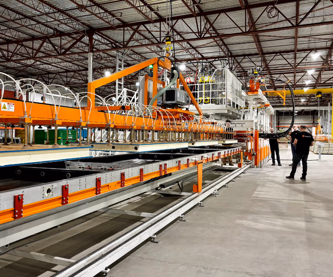 Grande machine industrielle orange et blanche dans un entrepôt avec deux hommes en t-shirts noirs à proximité.