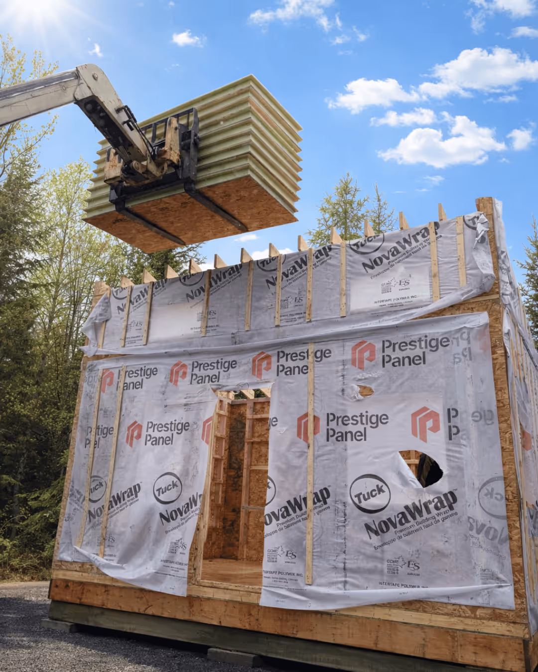Une grue soulève un panneau isolant au-dessus d'un bâtiment en construction enveloppé d'une membrane Prestige Panel NovaWrap.