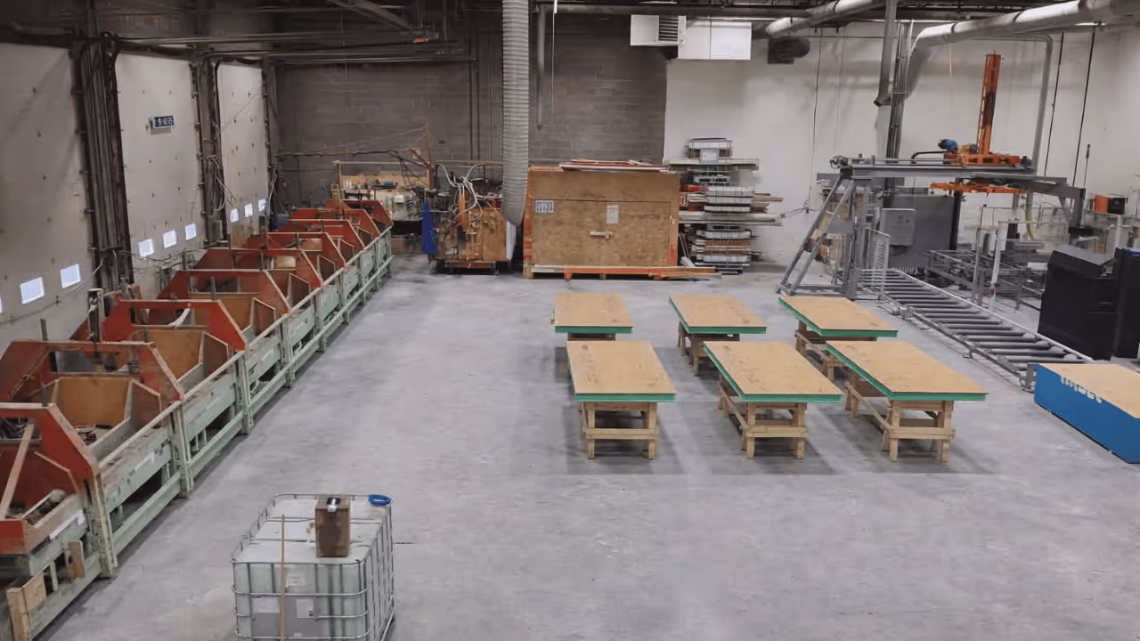 Chantier de construction en bois avec murs partiellement montés sur une fondation en béton entouré d'arbres verts.