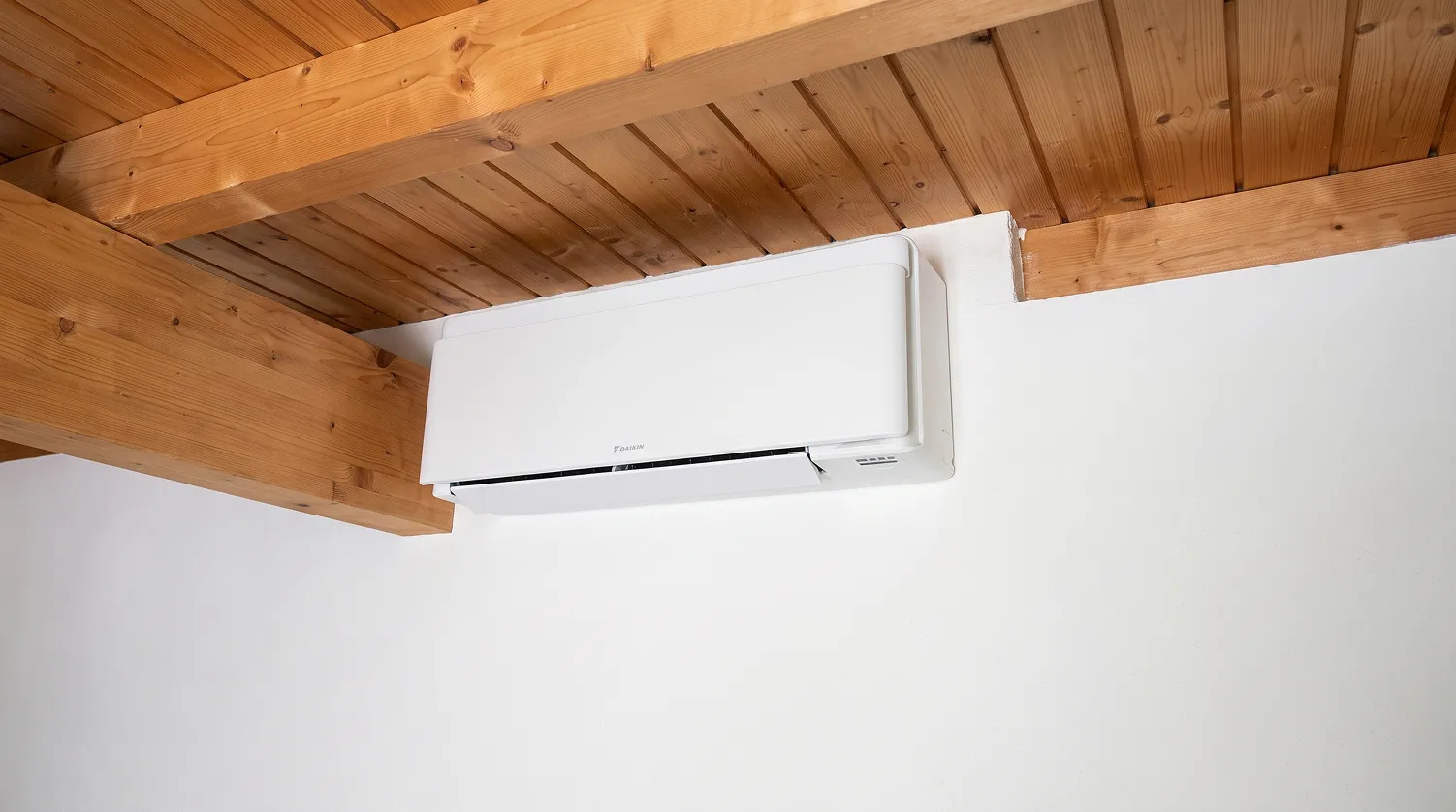 Weisses Innengerät an der Wand unter einer Holzbalkendecke