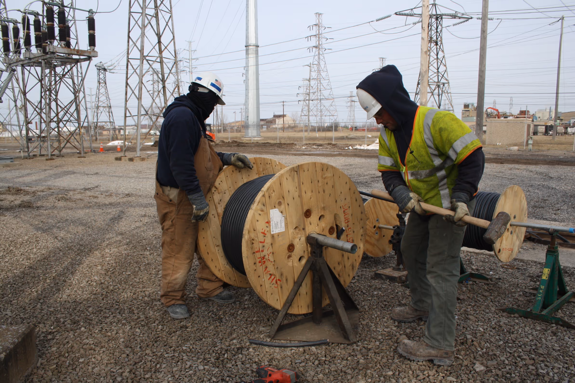 Electrical workers outdoors with large wire spool.