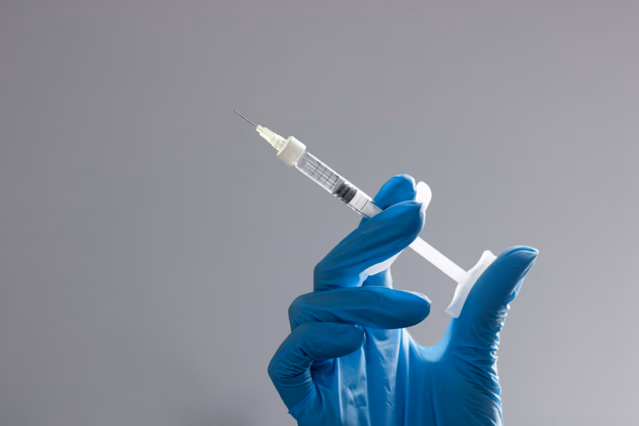 Hand in blue medical glove holding a filled syringe against a gray background.