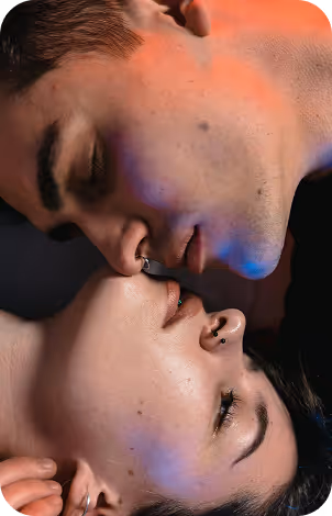 Close-up of a young couple lying face to face with eyes closed, illuminated by soft colored lighting.