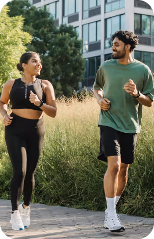 Young woman and man jogging together outdoors near greenery and modern buildings.