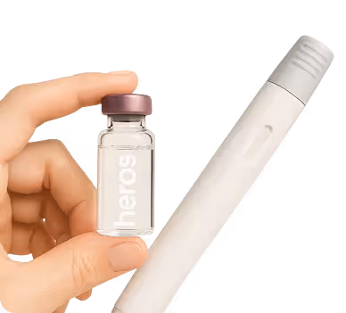 Hand holding a small glass vial labeled 'heros' next to a white pen-like medical device.