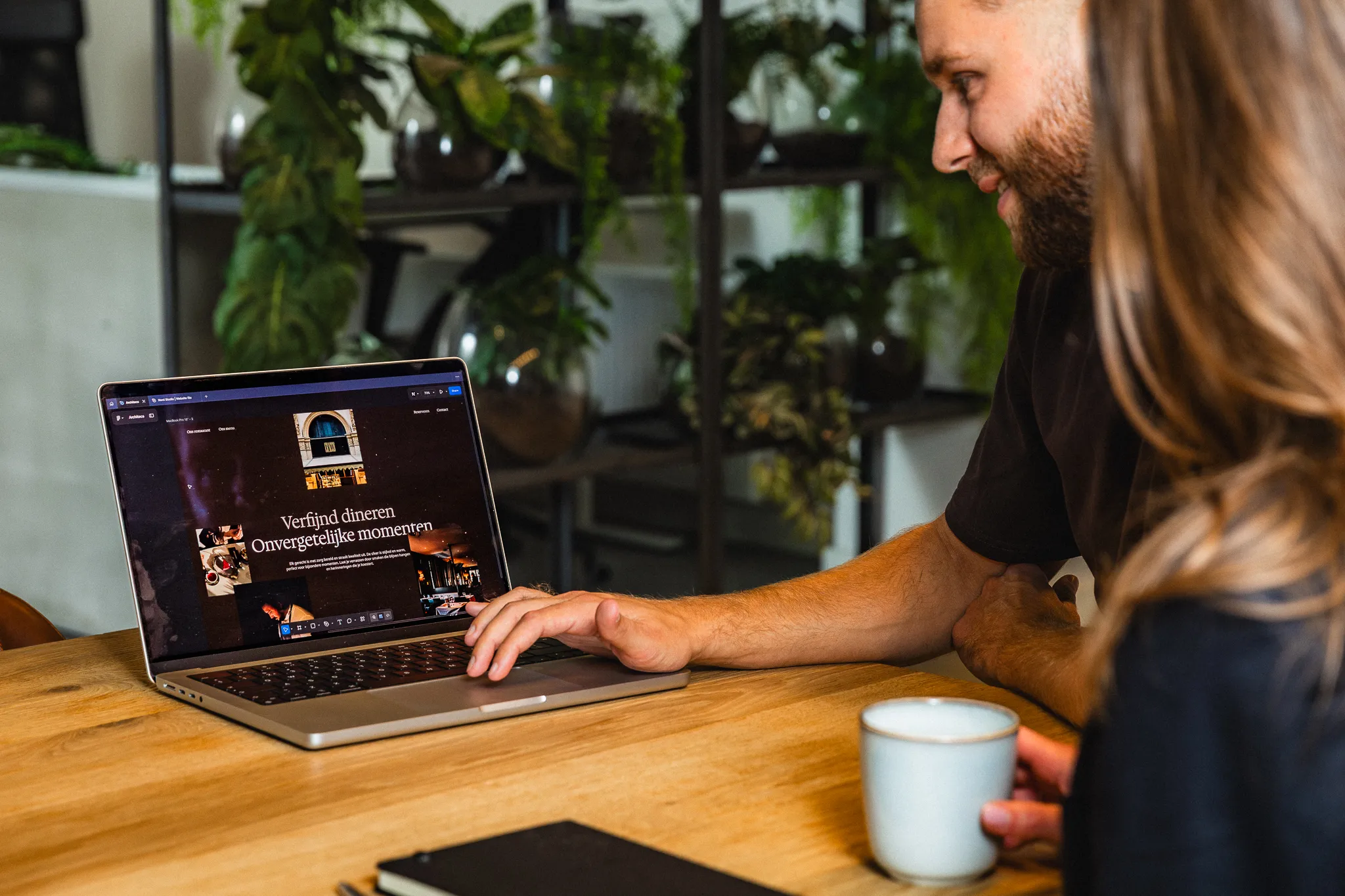 Uitleg over webdesign aan tafel met klant, met koffie en notities op tafel