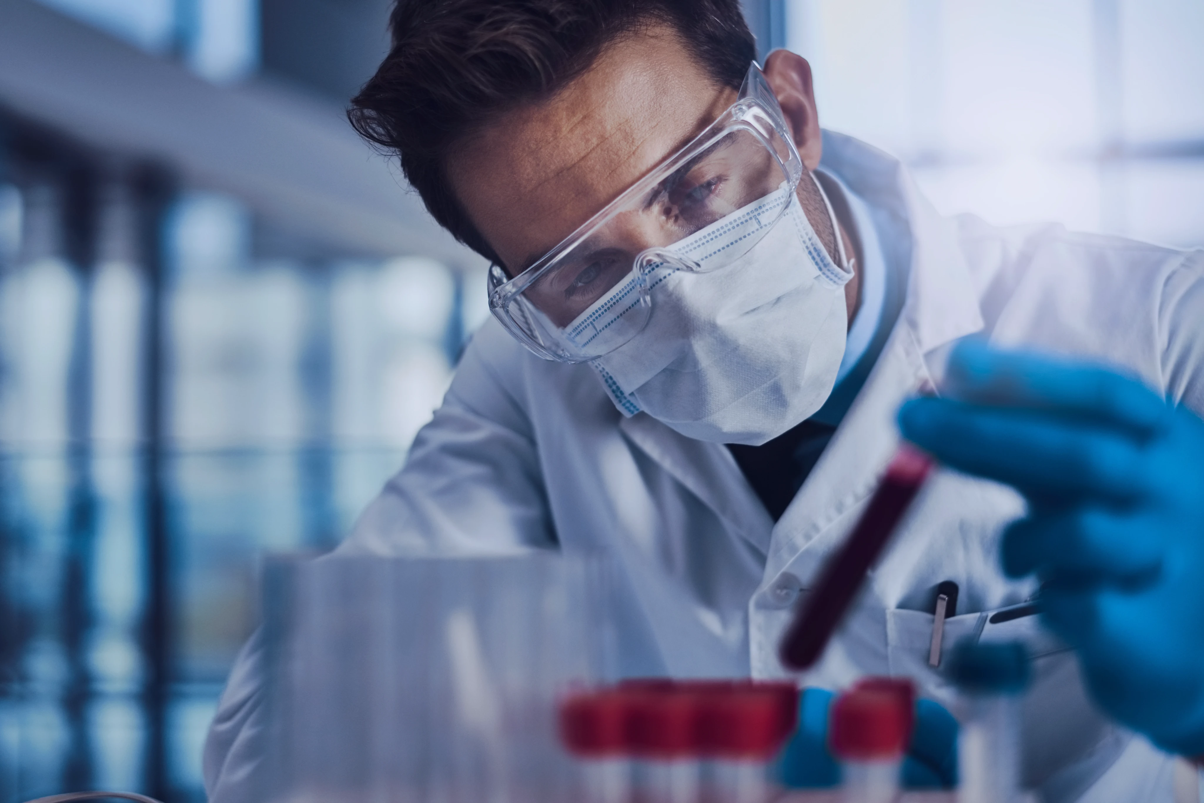 Scientist wearing glasses and mask handling blood vials