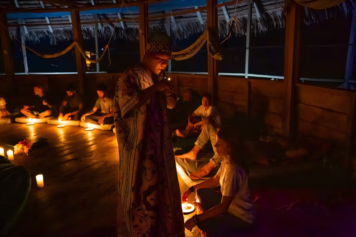 A shaman leads an intimate candlelit ritual as guests sit in quiet reverence, immersed in the ceremonial atmosphere.