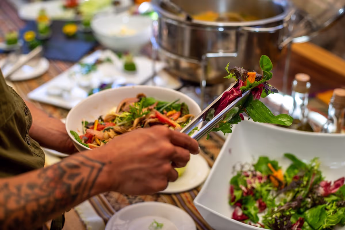 Close-up of colorful mixed salad being served from a buffet-style table with fresh greens, vegetables, and natural ingredients, reflecting dieta-friendly meals.