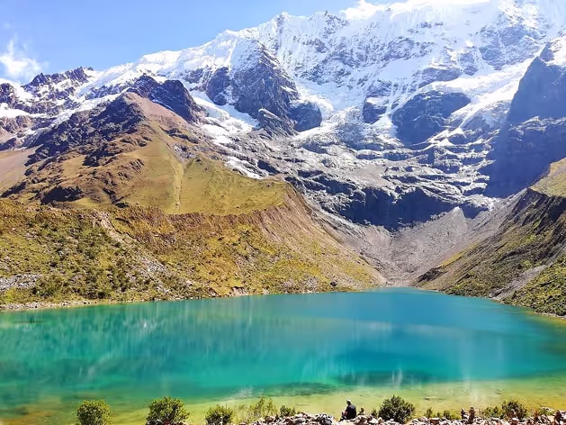 Vibrant turquoise lake surrounded by rugged mountains and snow-capped peaks under a clear blue sky in the Peruvian Andes.