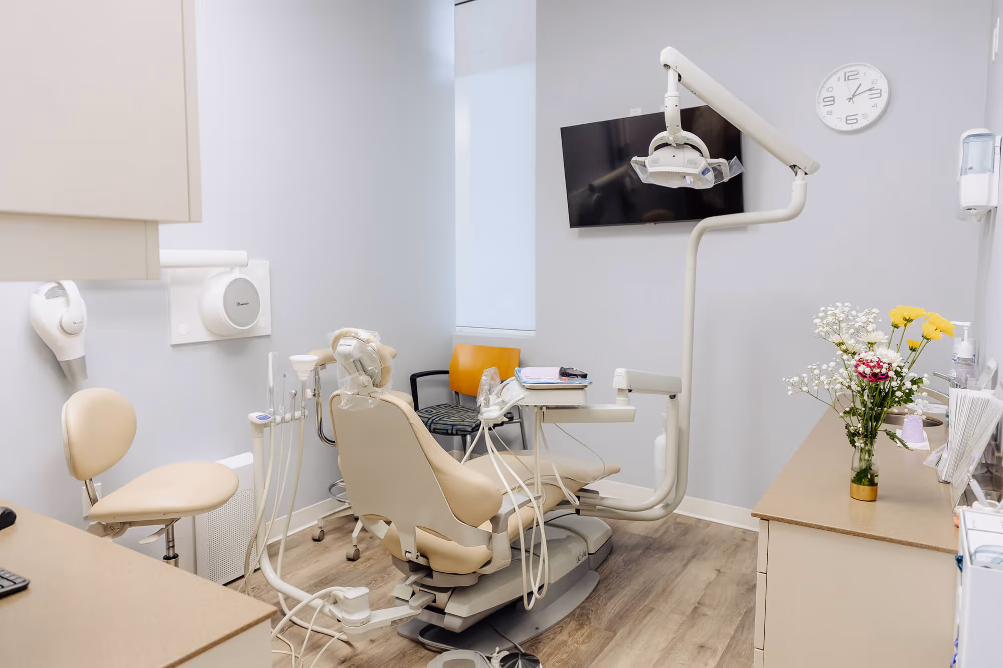 A dentist chair in a room with a flower in a vase.