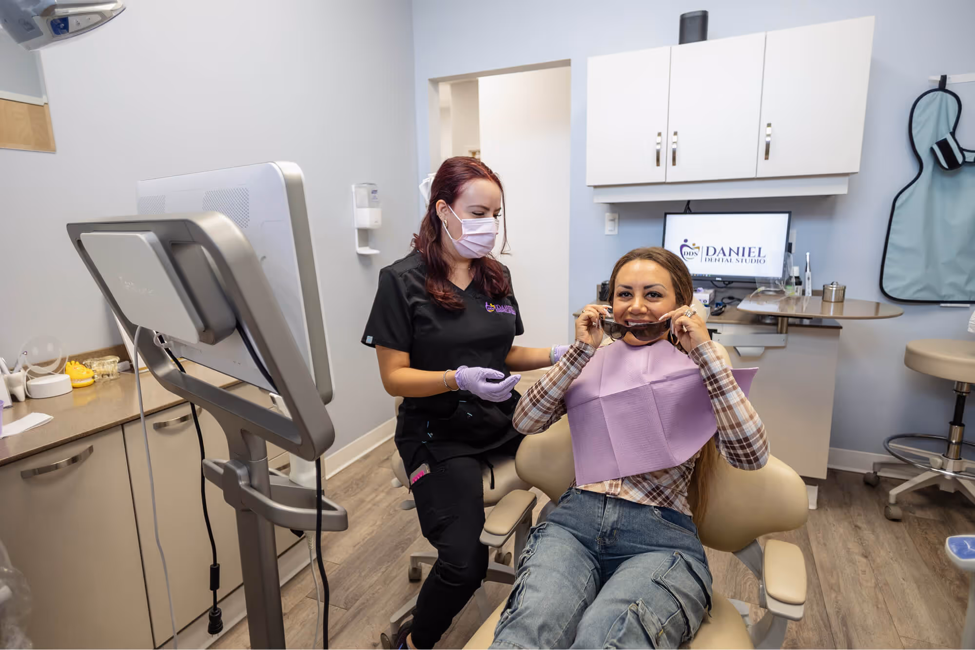 A woman sitting in a dentist chair while another woman holds a phone to her ear.