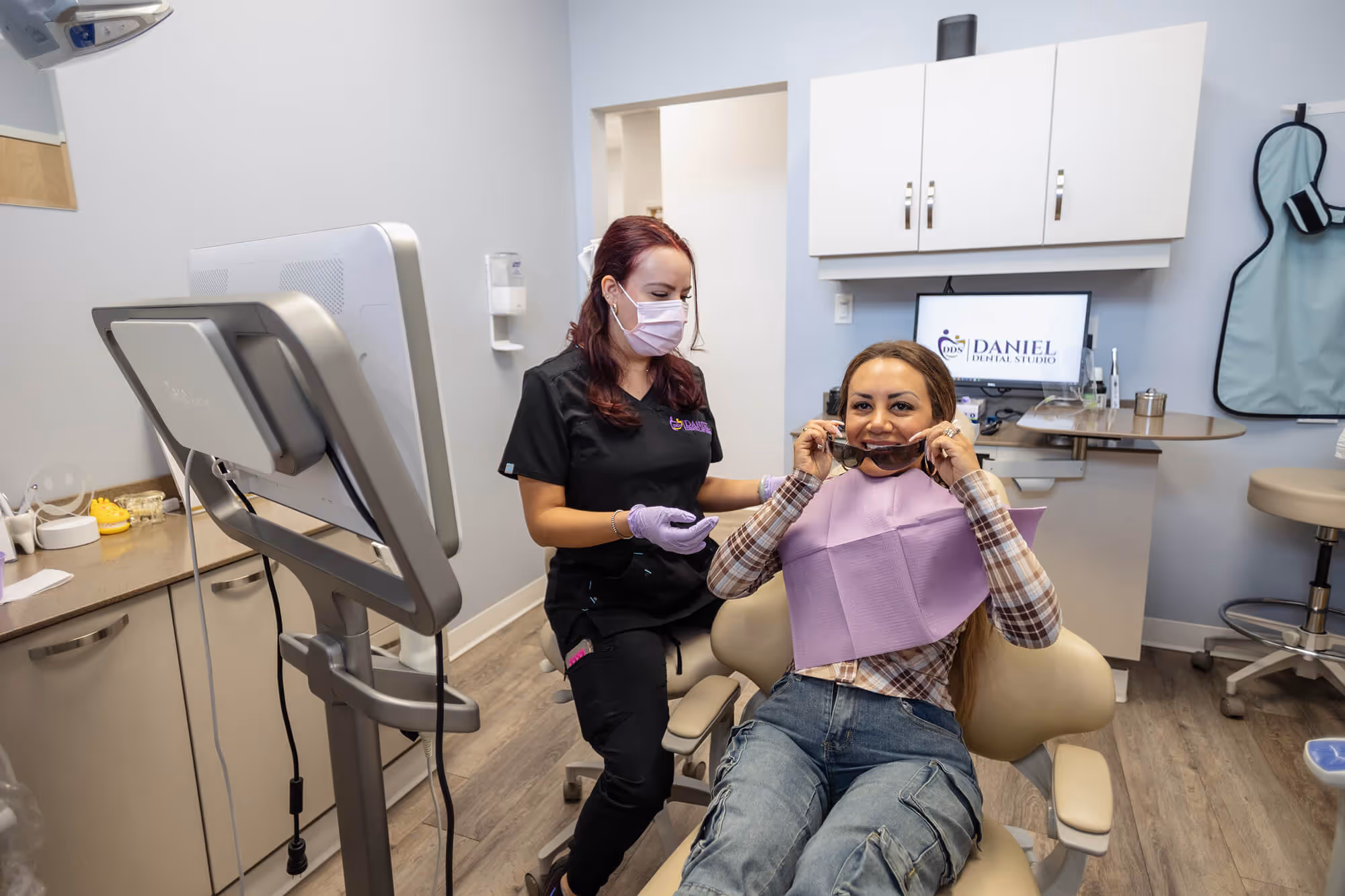 A woman sitting in a dentist chair while another woman stands behind her.
