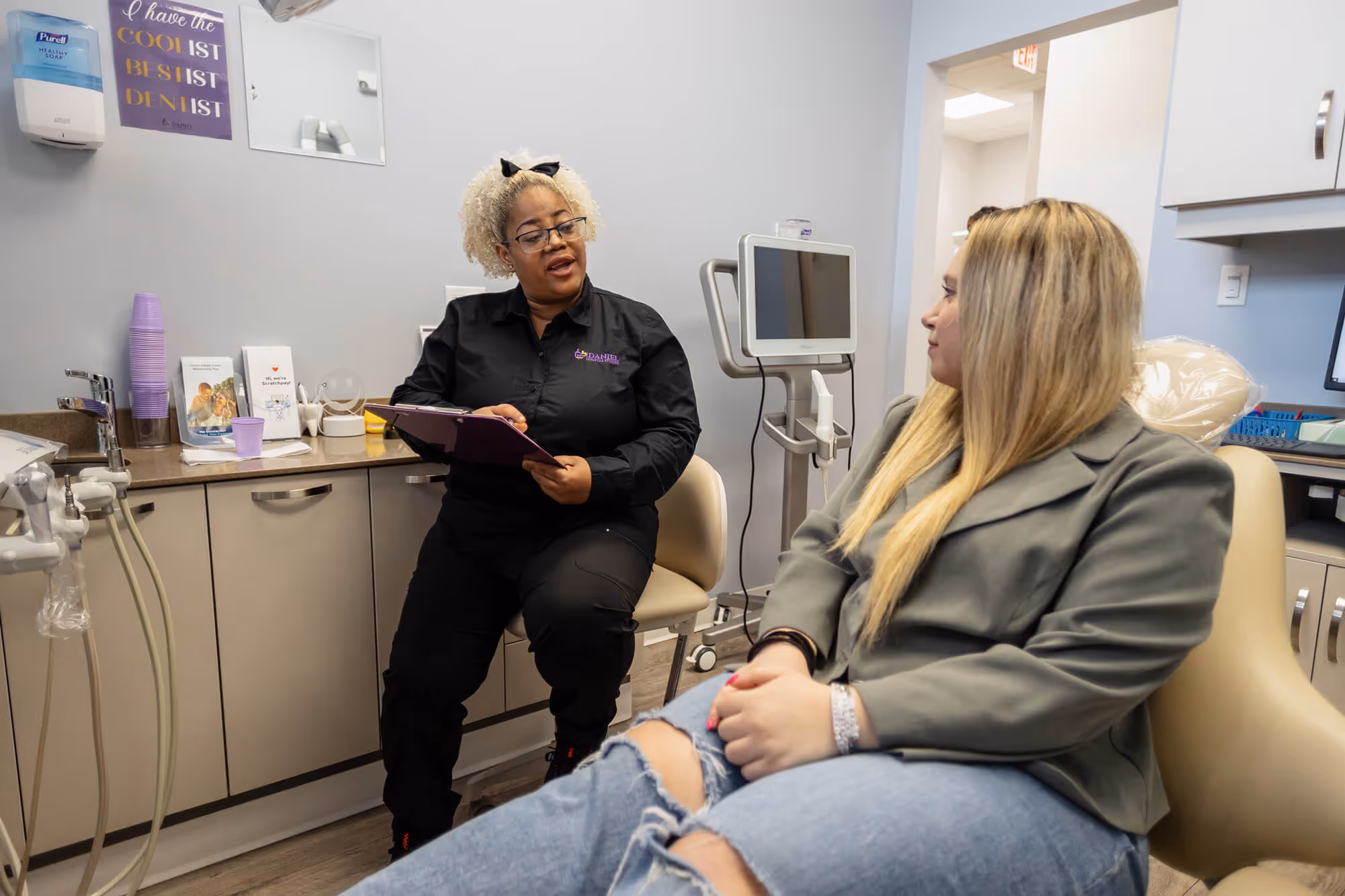 A woman sitting in a dentist chair talking to another woman.