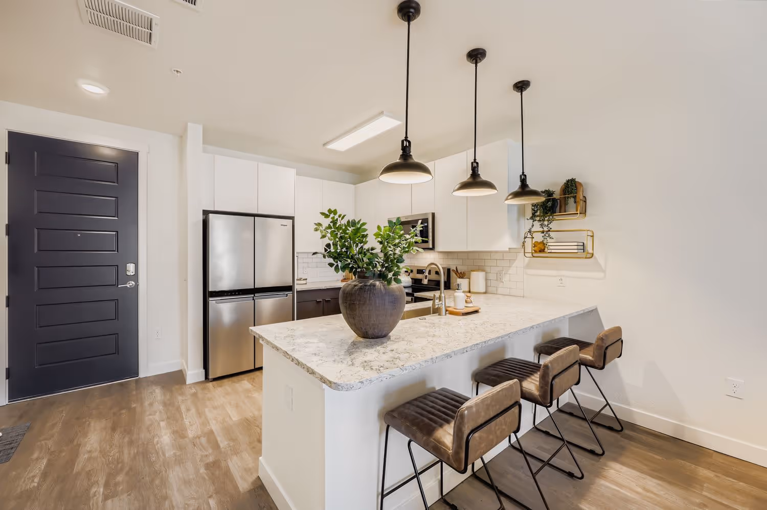 Modern apartment entryway and kitchen with white cabinets, a large island with bar seating, and stainless steel appliances at Avian Apartments in Colorado Springs, CO.