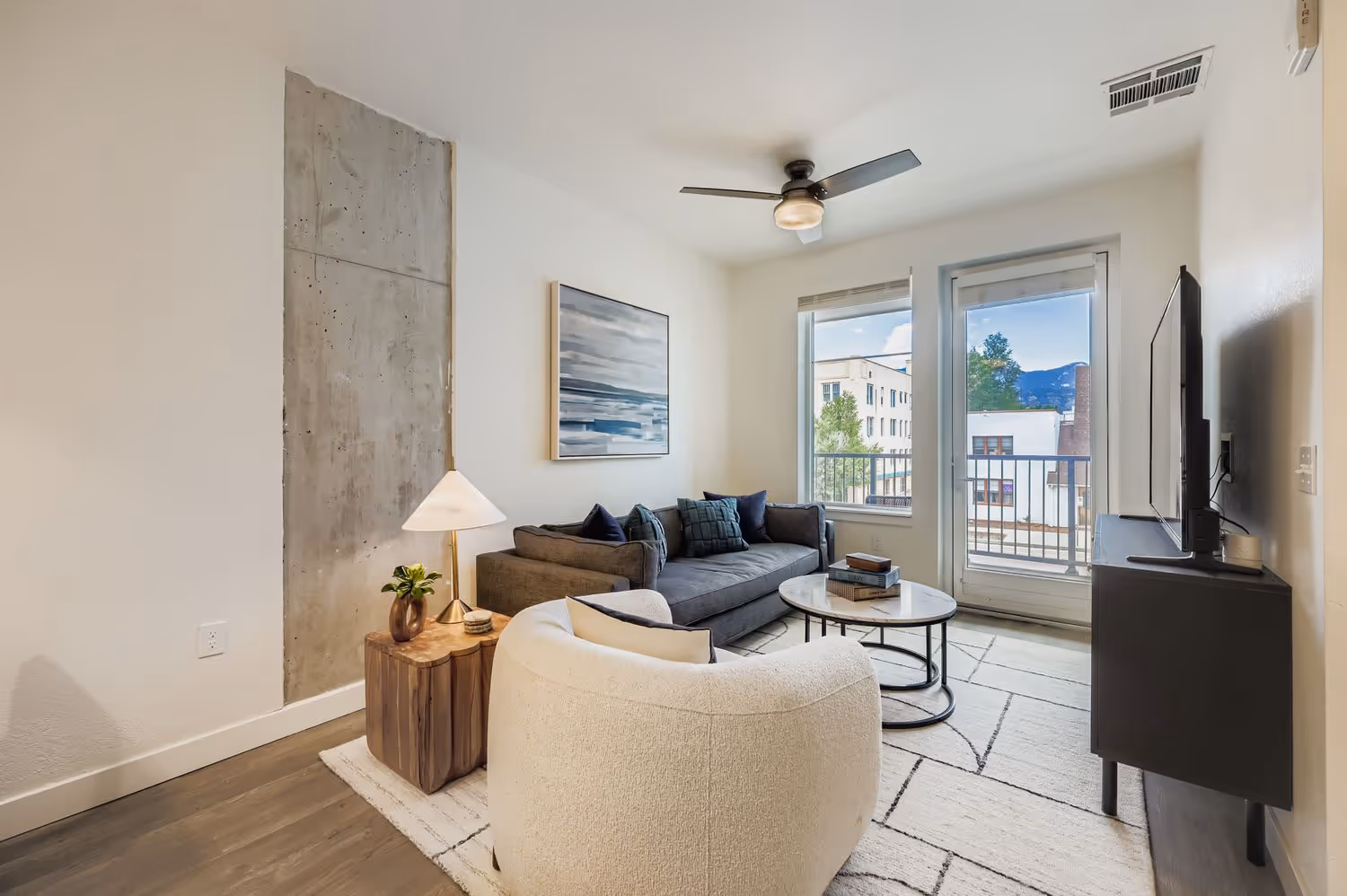 Bright apartment living room with a sofa, unique concrete accent wall, and a door leading to a private balcony at Avian Apartments in Colorado Springs, CO.