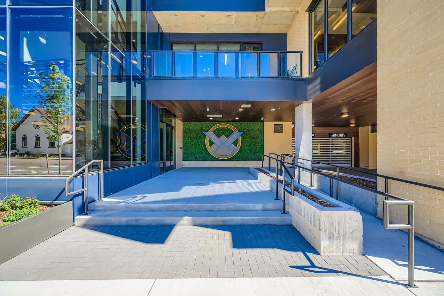 Modern apartment building entrance with a ramp, stairs, and the Avian logo against a green wall, leading to the resident garage in Colorado Springs, CO.