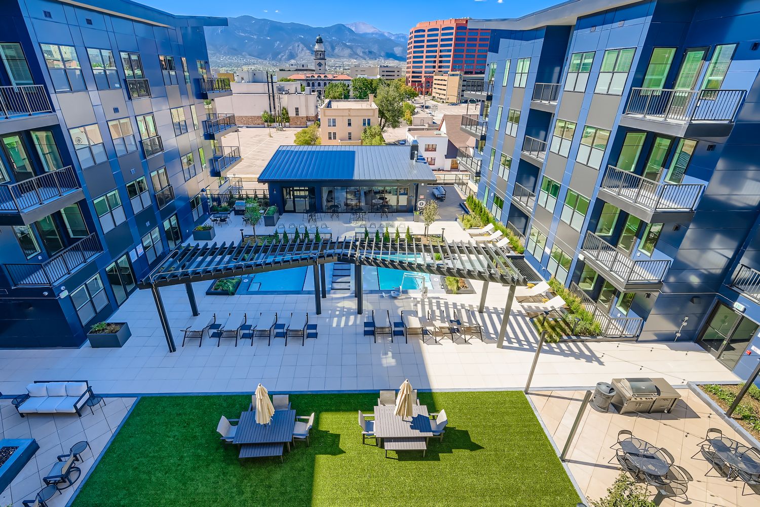 Aerial view of the modern Avian apartment buildings, showing the courtyard pool, sun deck, and outdoor grilling area with Pikes Peak in the background in Colorado Springs, CO