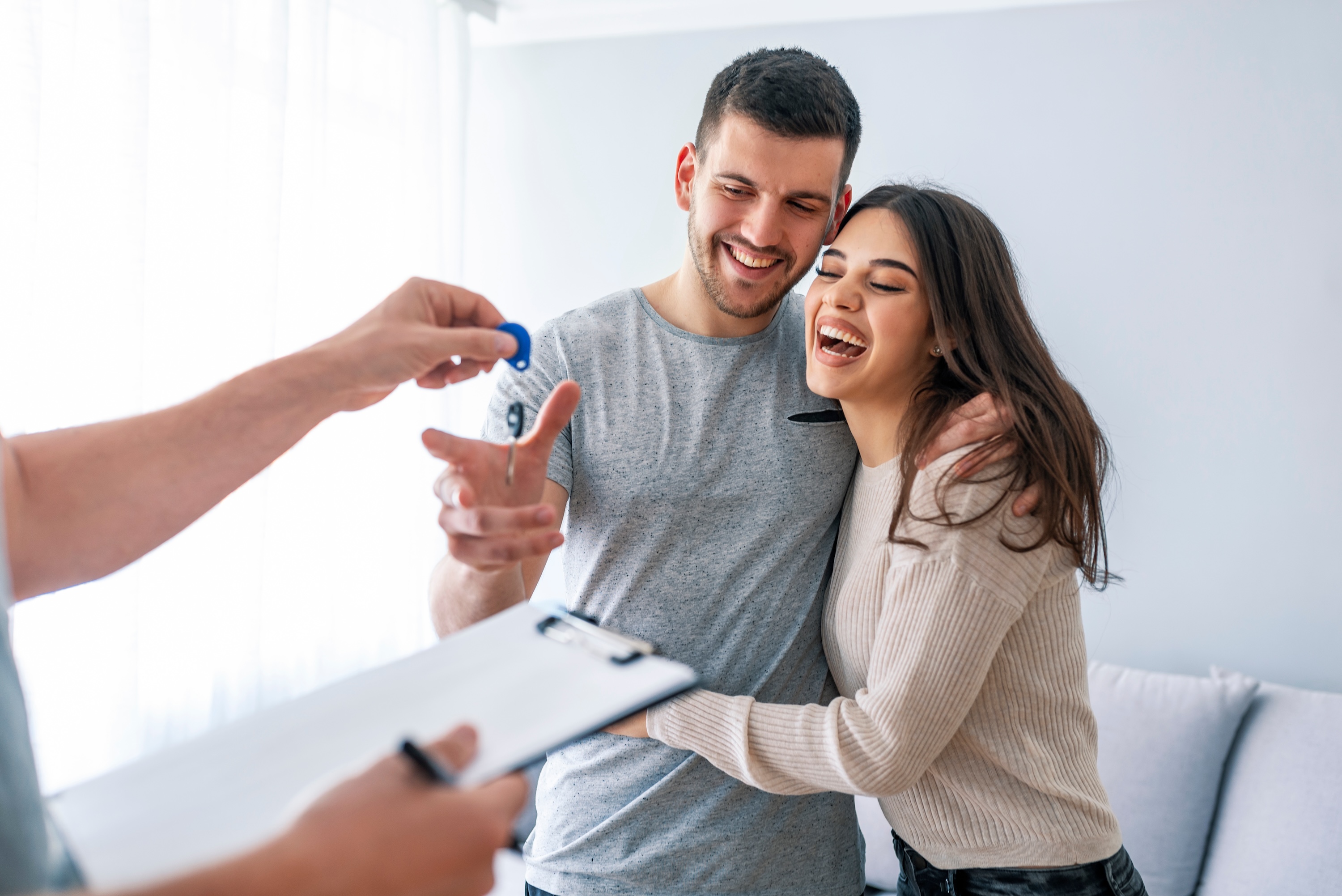 A happy couple embracing and smiling as they receive apartment keys from a leasing agent, celebrating their successful move-in to Avian Apartments in Colorado Springs, CO.