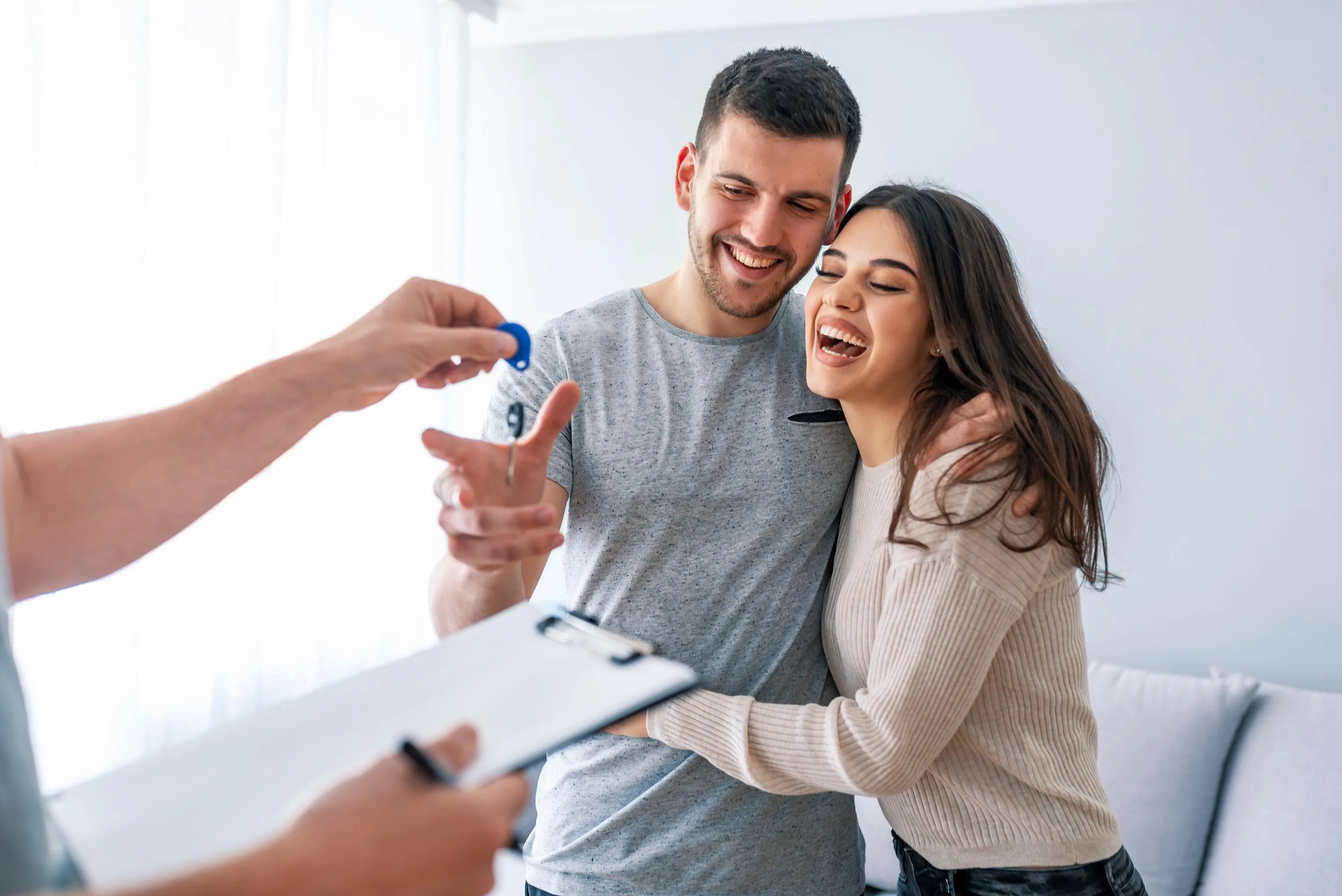 A happy couple embracing and smiling as they receive apartment keys from a leasing agent, celebrating their successful move-in to Avian Apartments in Colorado Springs, CO.