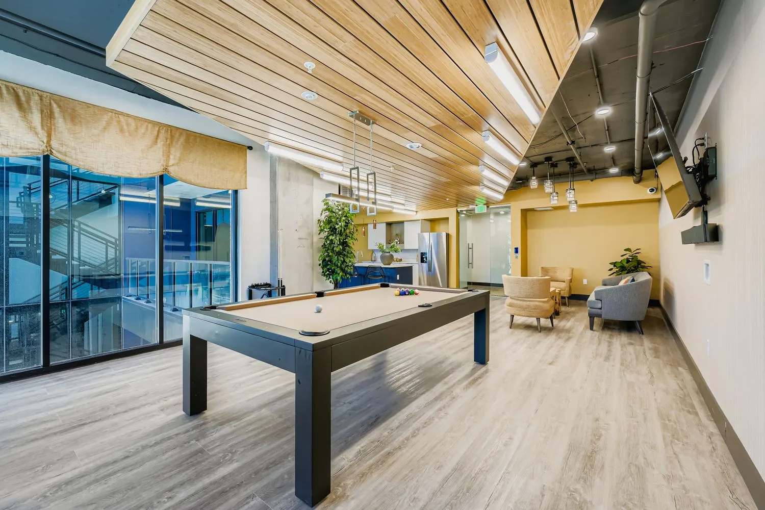 Resident game room and lounge area with a billiards table, modular seating, and an open view to the community kitchen at Avian Apartments in Colorado Springs, CO.