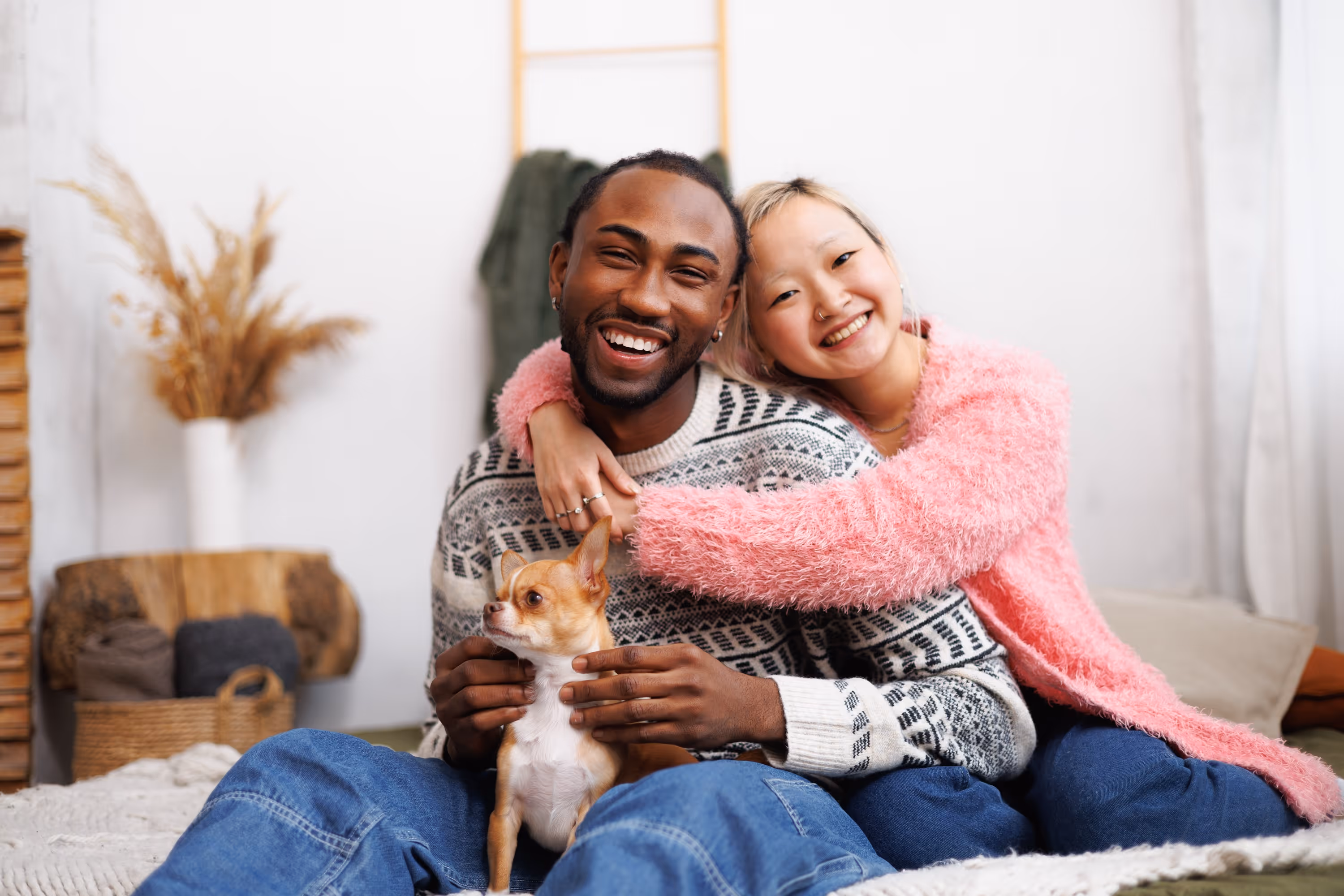 Happy couple sitting indoors on a bed at Avian Apartments, smiling and petting their small dog.