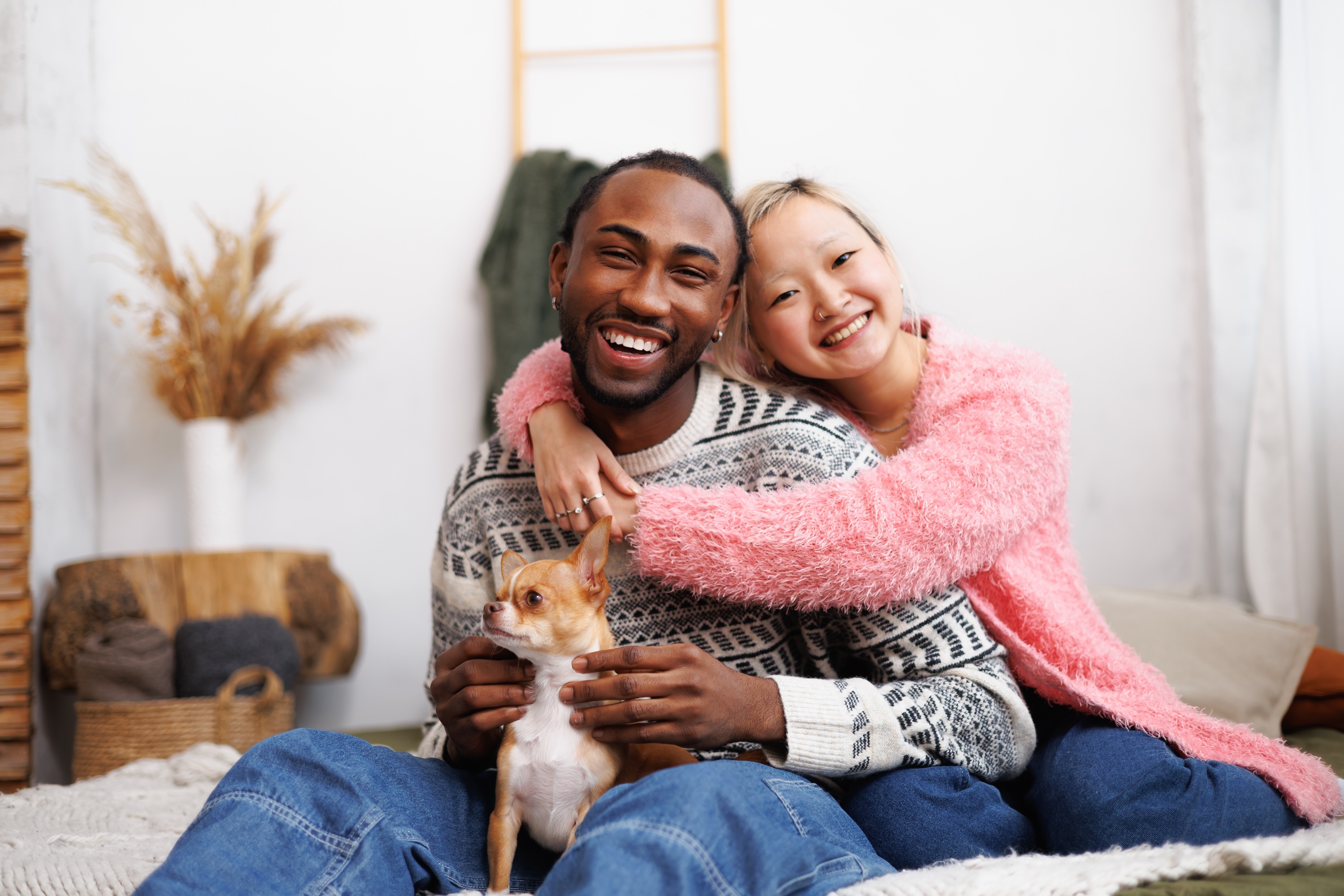 Happy couple sitting indoors on a bed at Avian Apartments, smiling and petting their small dog.