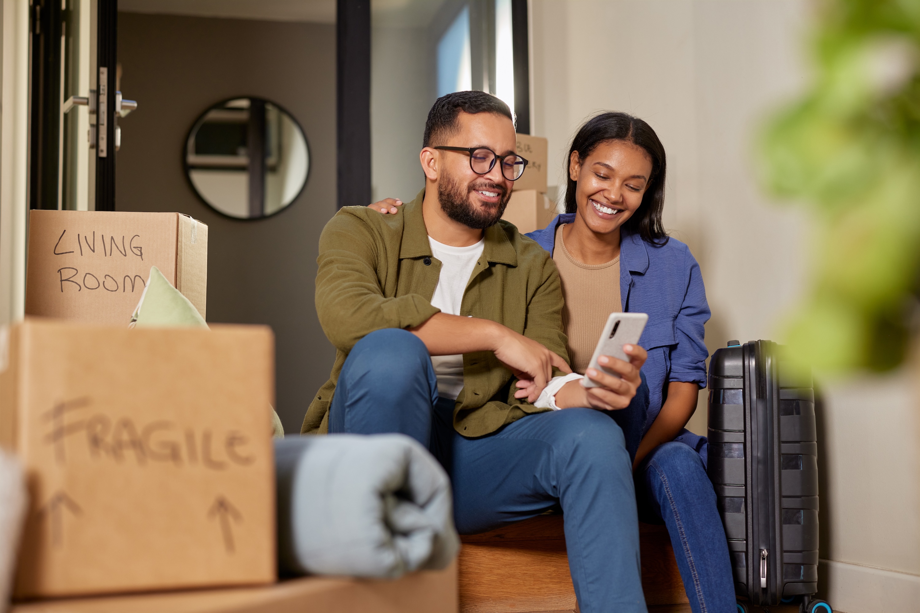 Smiling residents using a smartphone while surrounded by moving boxes at Avian Apartments in Colorado Springs, highlighting the community's move-in ready apartments.